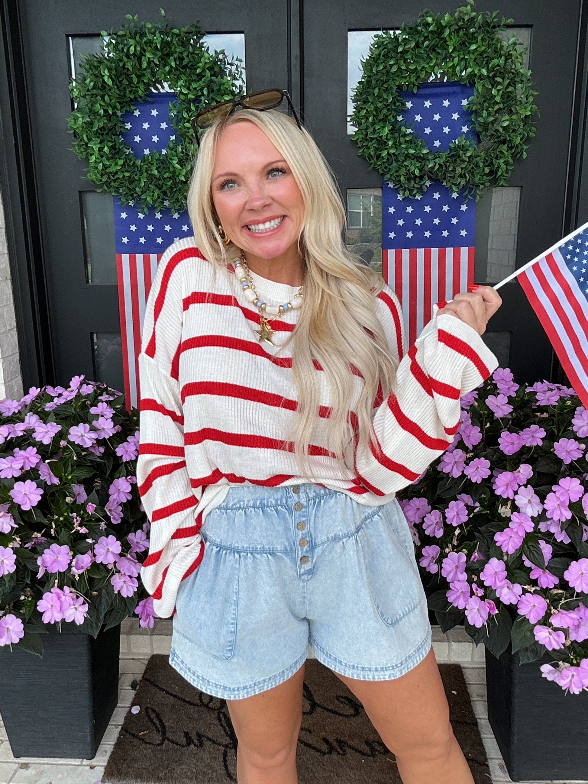 Woman wearing a red, white, and blue striped shirt with floral decorations and American flags in the background.